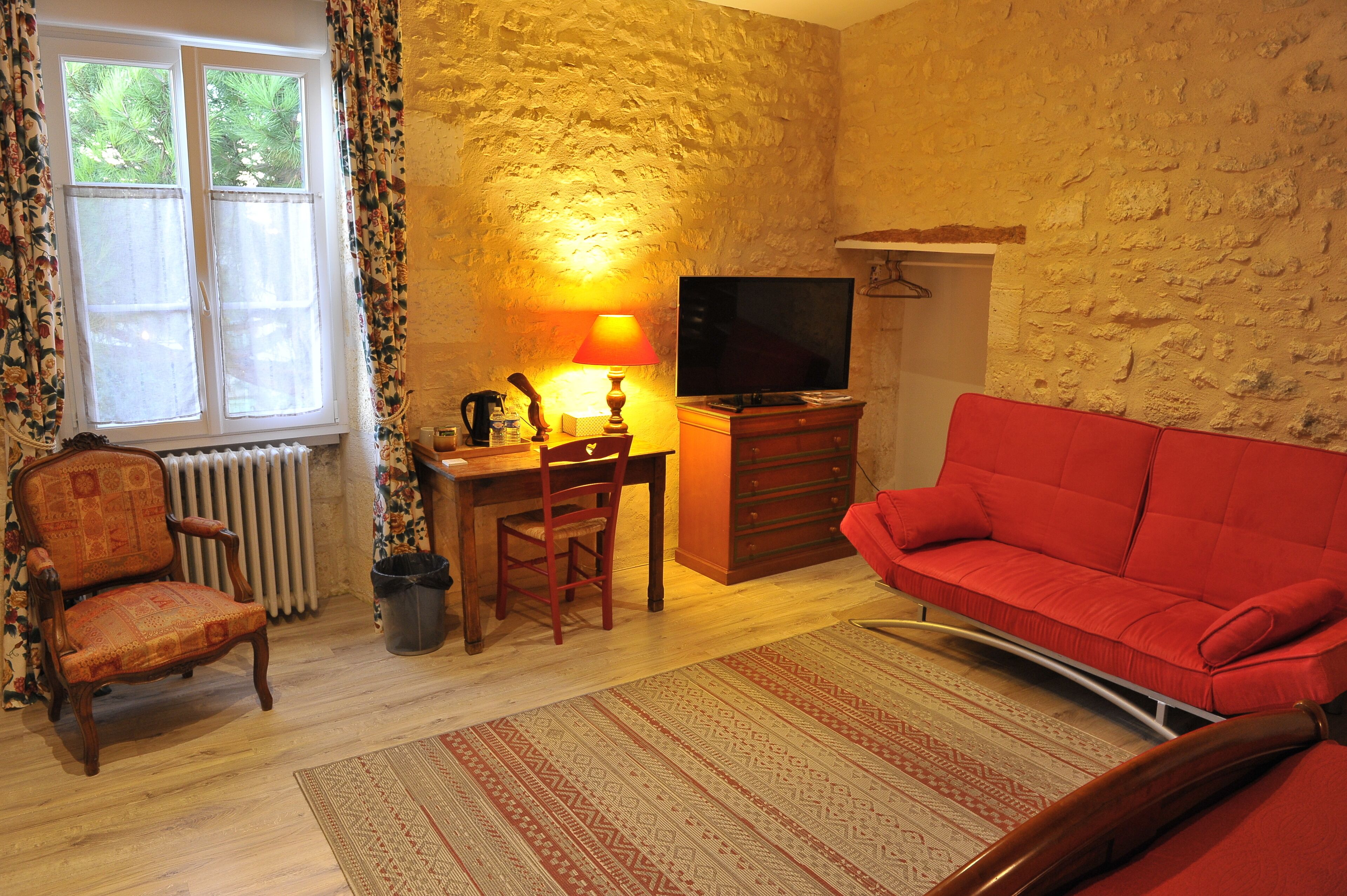 A cozy living room with a red sofa, a wooden chair, a small table with a lamp, and a television.