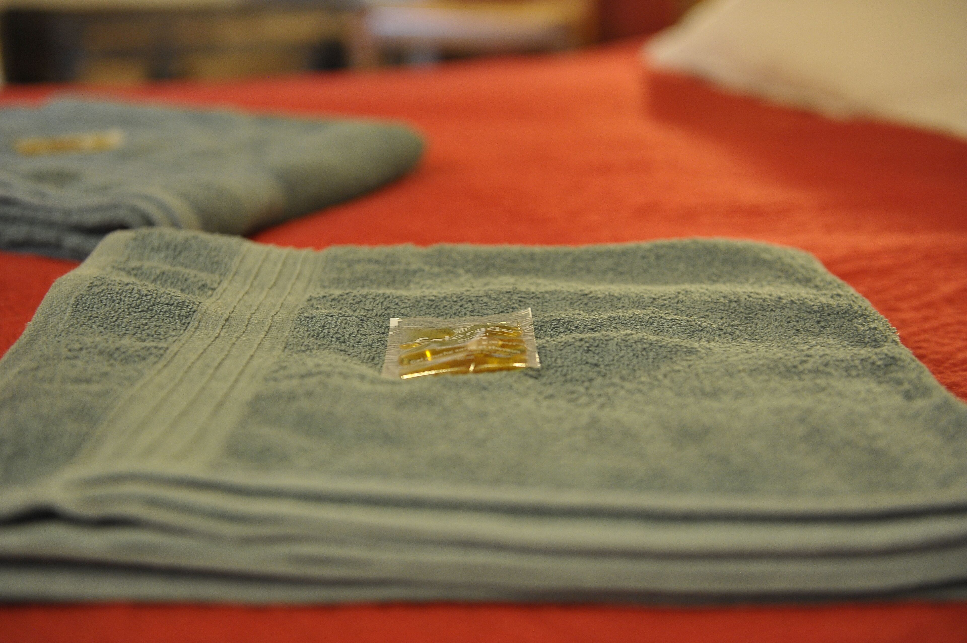 Une serviette soigneusement pliée sur un lit recouvert d’une couverture rouge.