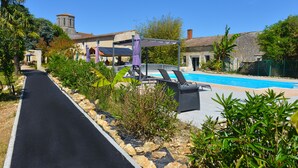 Un camino que lleva a una zona de piscina con sillones de descanso y una pérgola.
