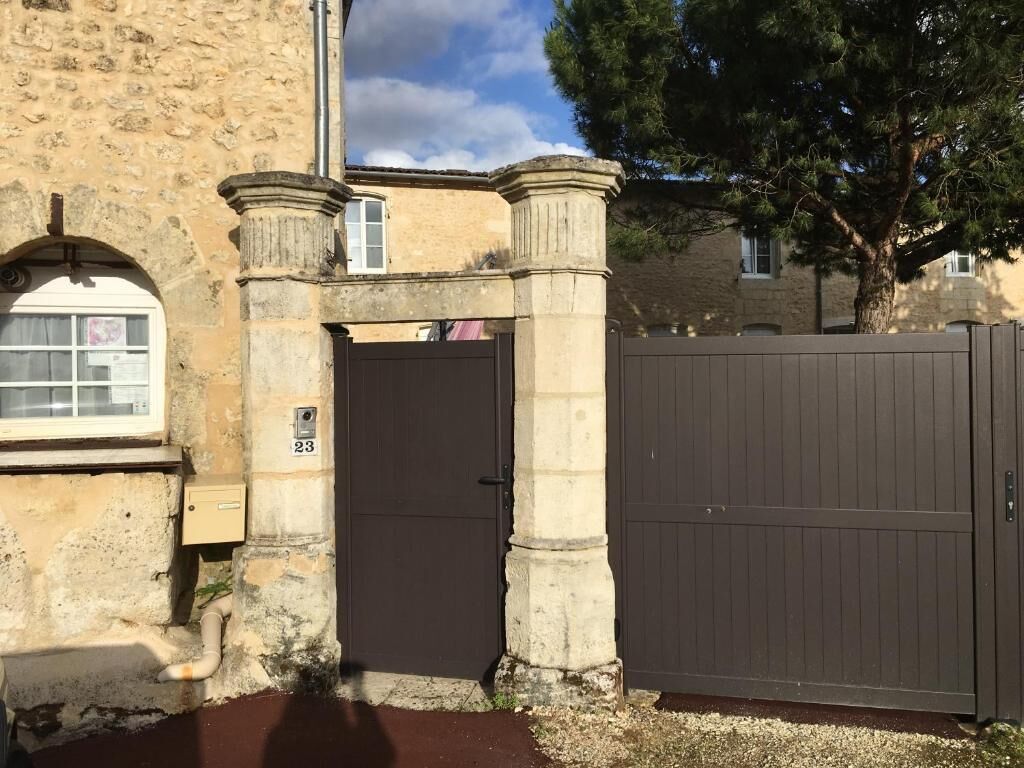 Una puerta de piedra con una placa de números, una puerta oscura cerrada y un árbol al fondo.