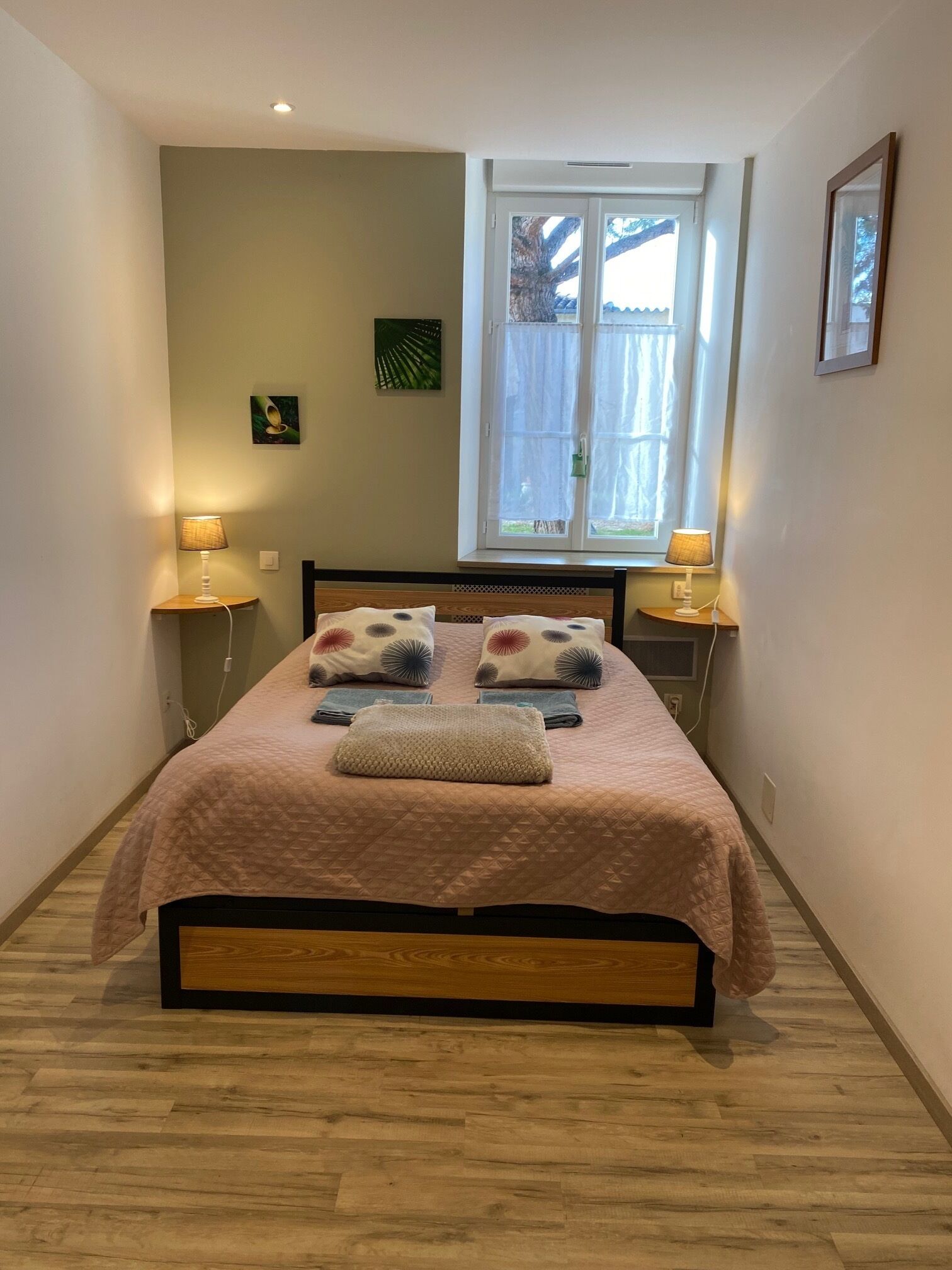 Un dormitorio ordenado con cama, dos lámparas de noche, una ventana con cortinas y una pequeña decoración en la pared.