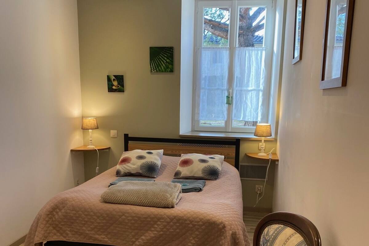 A bedroom with a bed, two bedside lamps, a chair, a window with curtains, and a wall-mounted picture.