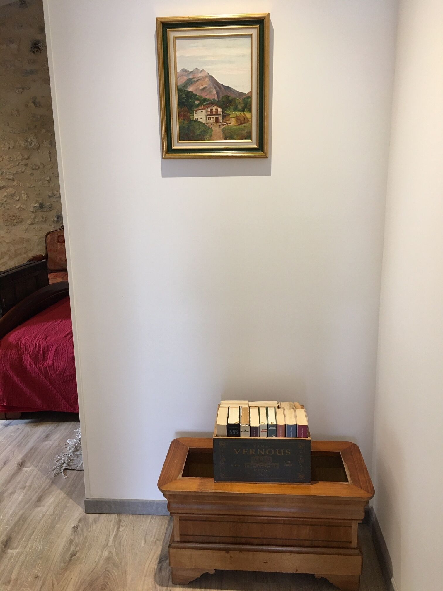 Una habitación con un aparador de madera, un cuadro enmarcado de un paisaje montañoso y una cama roja.