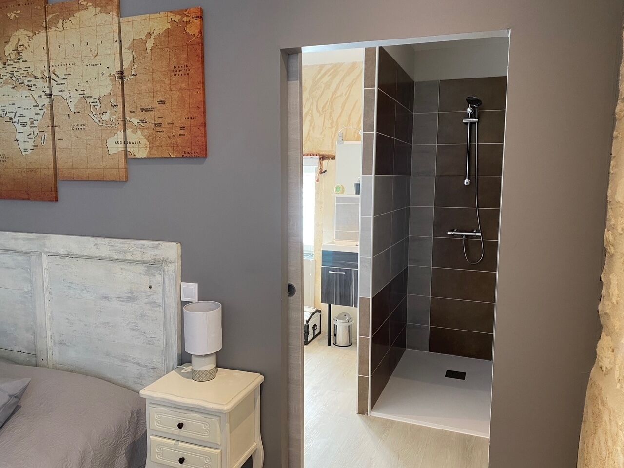 A bedroom with a bed, a nightstand, a map on the wall, and a bathroom with a shower.