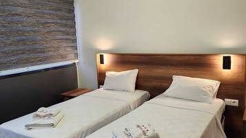 A hotel room with two beds, each with a neatly folded towel and a pillow. The room has a modern design with a wooden headboard and a wall-mounted light fixture.