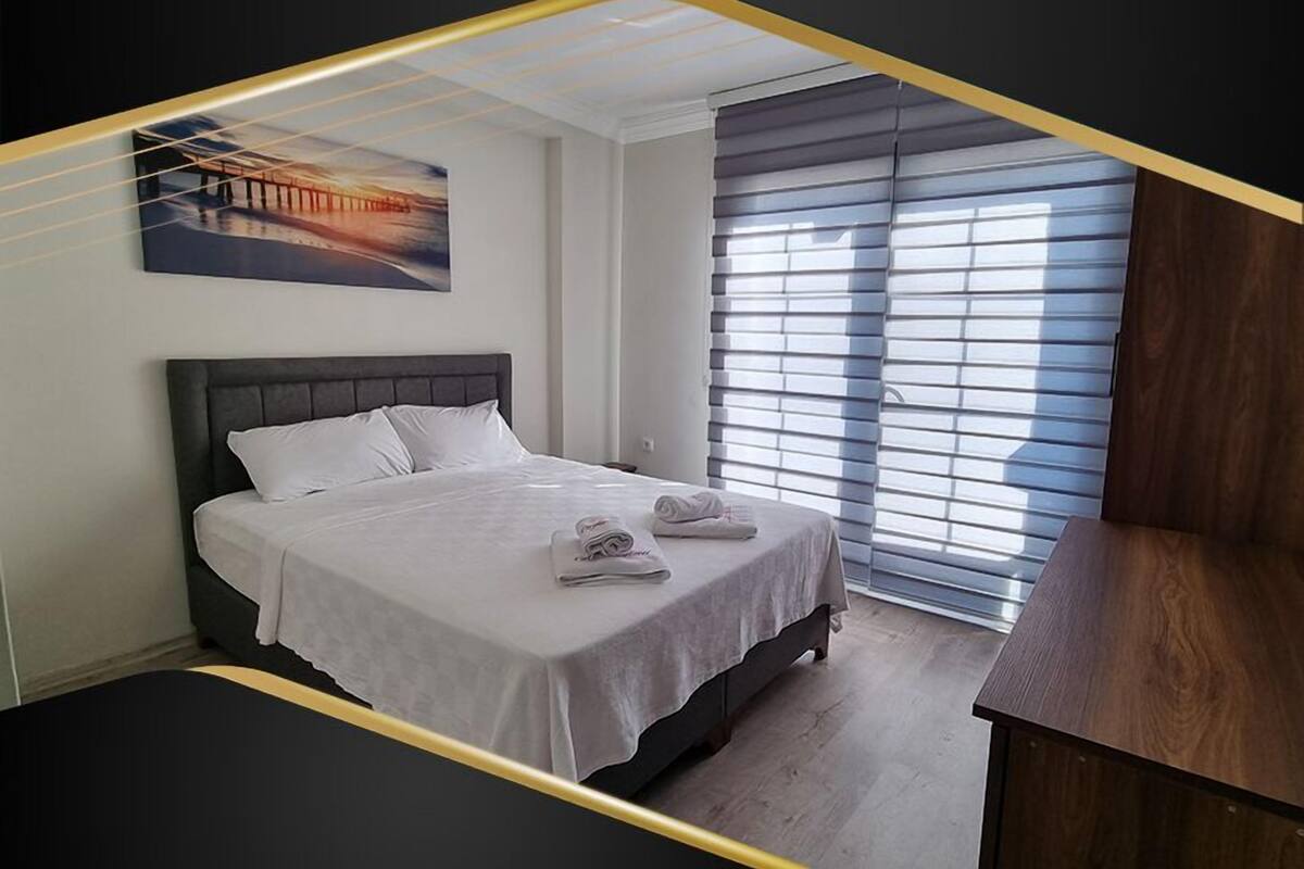 Un dormitorio con cama, una mesita de noche, una ventana con persianas y un cuadro en la pared.