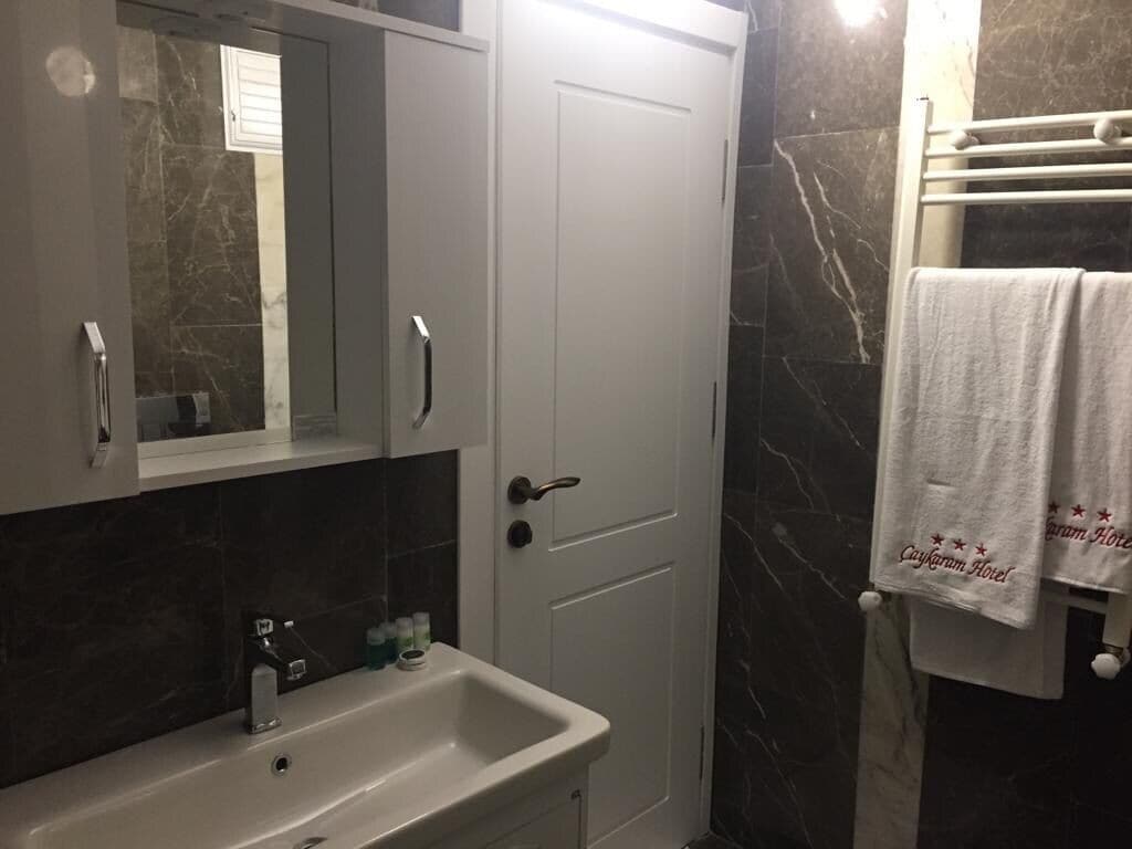 A bathroom with a white sink, a mirror, a door, and a towel rack with towels.