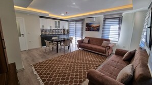Una sala de estar moderna con un tapete marrón estampado, un sofá marrón y una zona de comedor con una mesa de vidrio y sillas.