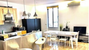 Une cuisine moderne dotée d’un îlot central, de tabourets de bar, d’une table à manger avec des chaises et d’un téléviseur.