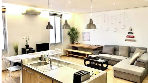 Une cuisine moderne avec un îlot central, un coin repas avec un banc et un salon avec un canapé.