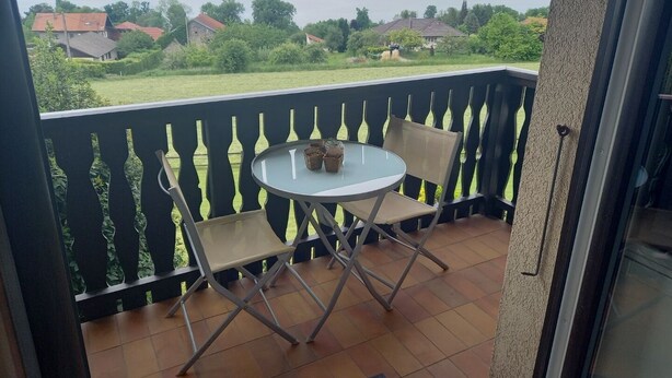 A balcony with a table and two chairs, overlooking a lake and houses. - Location Saisoniere au Calme Dans Petite Copropriete (Publier)