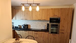 A kitchen with wooden cabinets, a countertop with appliances, and a dining area with a table and chairs. - Location Saisoniere au Calme Dans Petite Copropriete (Publier)