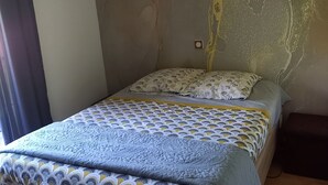 A bedroom with a bed, a wall with a textured design, and a ceiling light. - Location Saisoniere au Calme Dans Petite Copropriete (Publier)