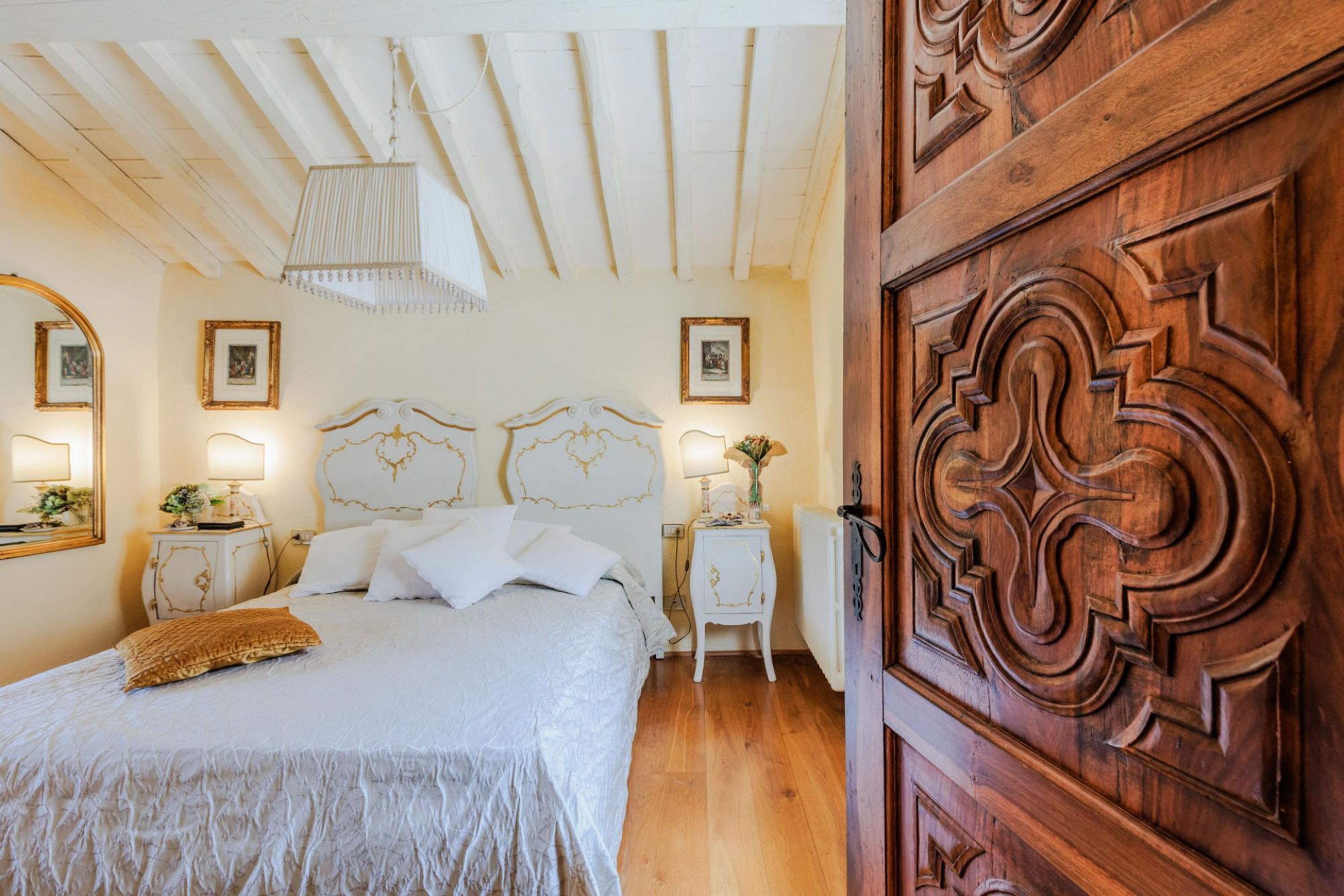 A bedroom with a bed, nightstands, a mirror, and a wooden door.
