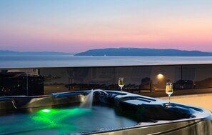 Een hottub met een groen licht, twee glazen wijn en uitzicht op de oceaan bij zonsondergang.