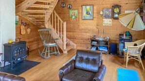 Un interior de cabaña acogedor con una escalera de madera, una mecedora, un sofá de cuero y una pequeña mesa con velas.