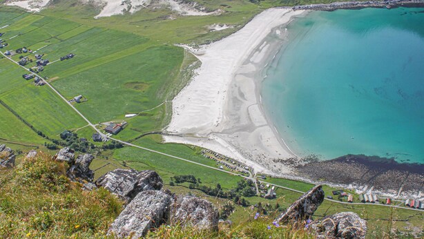 Un paisaje costero con una playa arenosa, campos verdes y un primer plano rocoso.