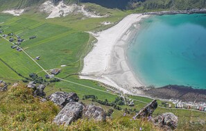 Un paysage côtier avec une plage de sable, des champs verdoyants et un premier plan rocheux.