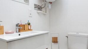 Een moderne badkamer met een witte wastafel, houten opbergruimte, een toilet en een spiegel.