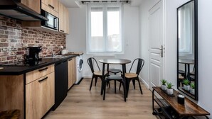 Een moderne keuken met een tegelwand, houten kastjes, een zwart aanrecht en een eethoek met een ronde tafel en stoelen.