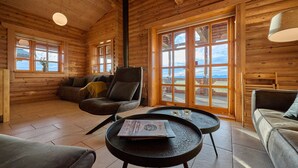 Interior acollidor d'una cabana amb parets de fusta, un sofà, una cadira i una taula amb un llibre.
