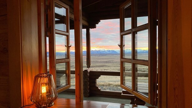 Habitació amb grans finestres que donen vista a un paisatge montanyós durant el capvespre.