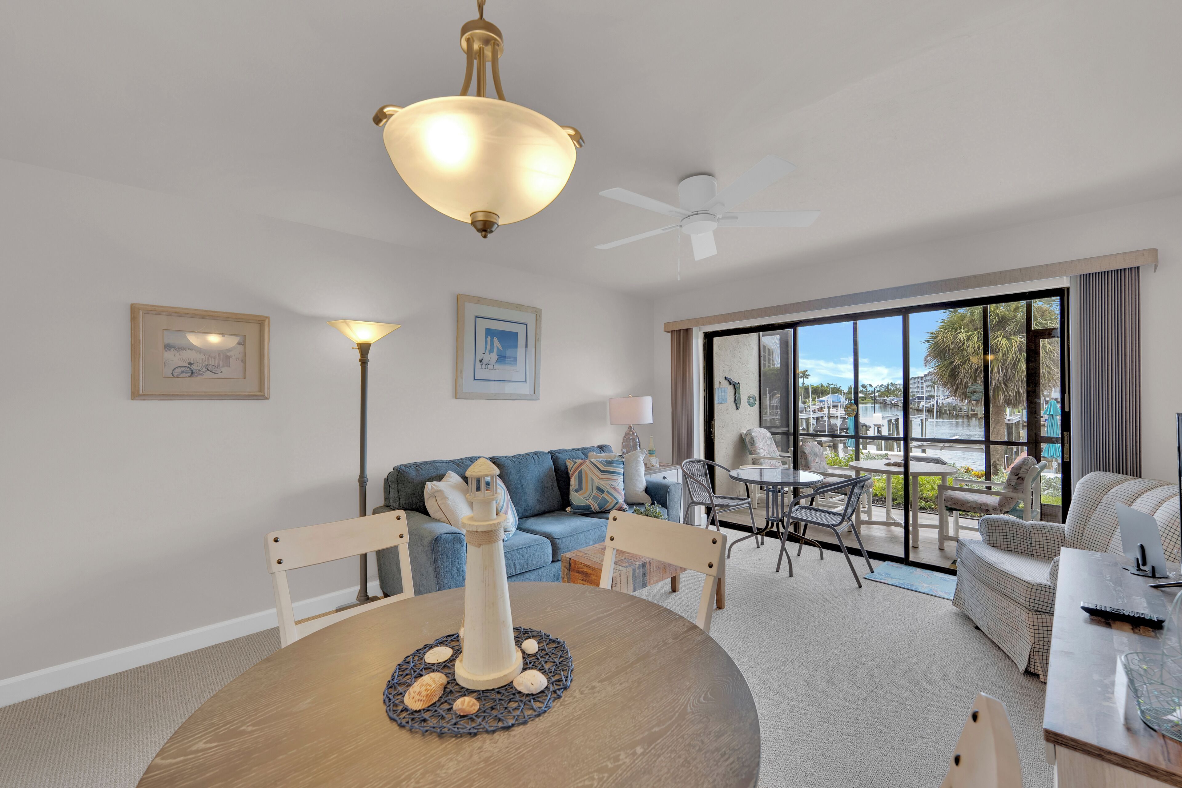 A modern living room with a dining table, a blue sofa, and a view of an outdoor pool area.