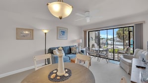 Ein modernes Wohnzimmer mit Esstisch, einem blauen Sofa und Blick auf einen Außenpool.