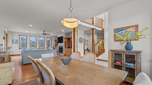 A spacious living area with a wooden dining table, a sofa, and a staircase leading to an upper level. - 1603 - Bare Feet Retreat - Pet-Friendly Corolla Retreat Near the Beach (Corolla)