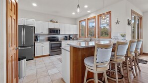 A modern kitchen with white cabinets, stainless steel appliances, and a wooden island with bar stools. - 1603 - Bare Feet Retreat - Pet-Friendly Corolla Retreat Near the Beach (Corolla)
