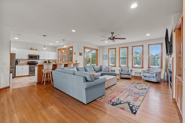 A spacious living area with a grey sectional sofa, a patterned rug, and a ceiling fan.