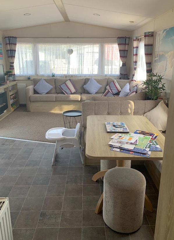 A cozy living area with a sofa, a dining table, and a small kitchen area. - Beautiful caravan located opposite Greatstones stunning beach (Greatstone)