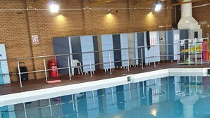 Een binnenzwembad met betegelde vloer en wanden, een bakstenen muur op de achtergrond en een brandblusser aan de linkerkant.