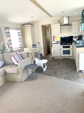 A compact living space with a kitchenette, a sofa, a small dining table, and a compact kitchen area. - Beautiful caravan located opposite Greatstones stunning beach (Greatstone)