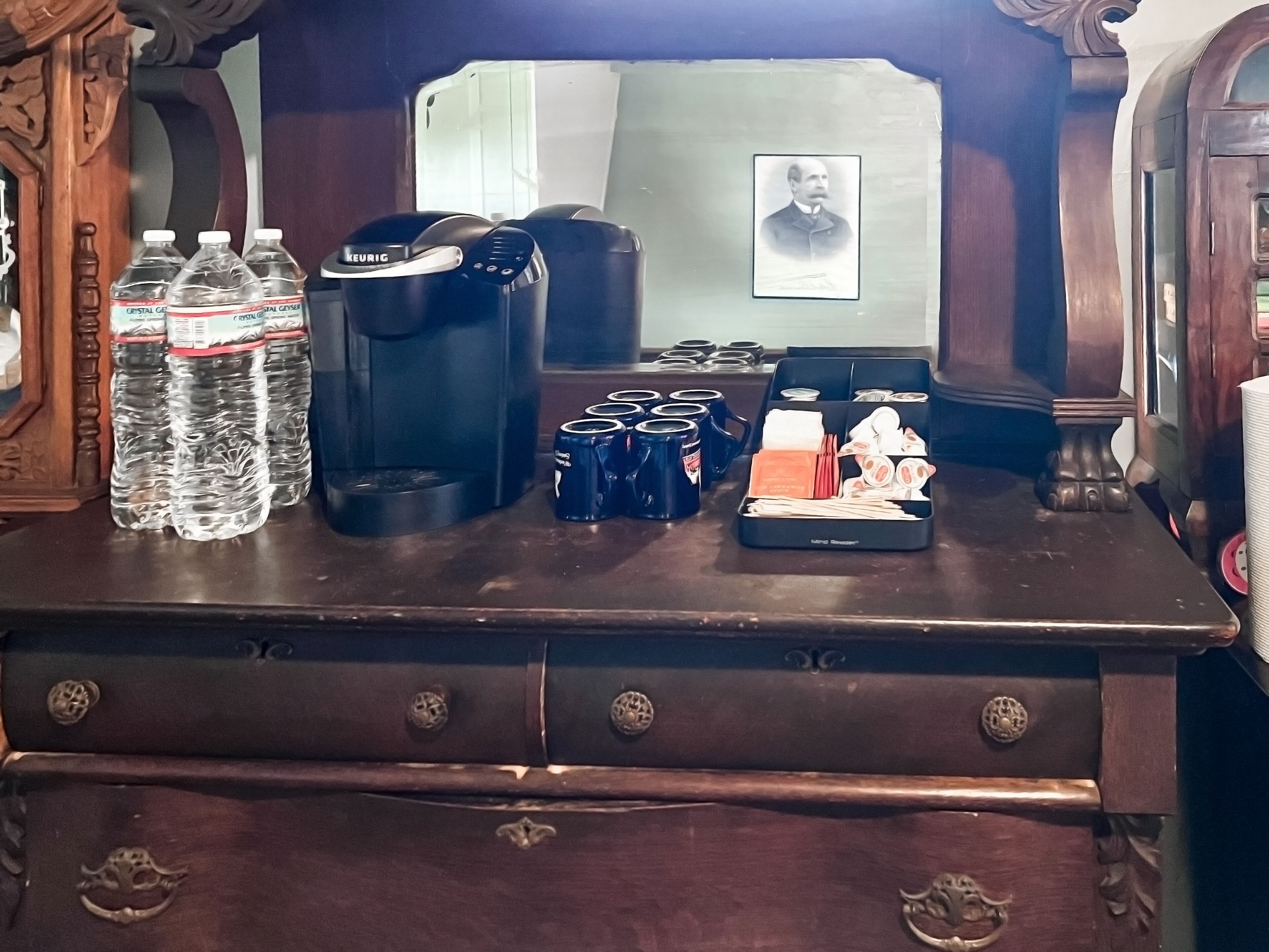 En kaffestation med en kaffebryggare, flaskor med vatten och ett mugghållare.