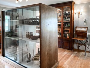 Um quarto com um armário de vidro que exibe vários objetos, um móvel de madeira com portas de vidro e uma cadeira de estilo antigo.