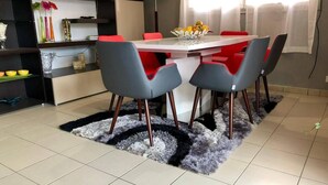 Un comedor con una mesa blanca y cuatro sillas grises con cojines rojos.