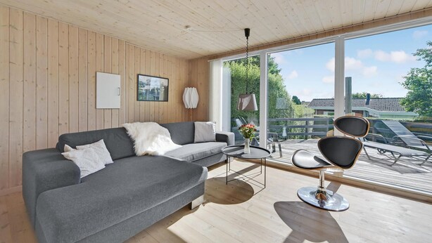 Una sala de estar moderna con un sofá gris, una mesa redonda y una silla negra. Una ventana grande ofrece vistas al exterior.