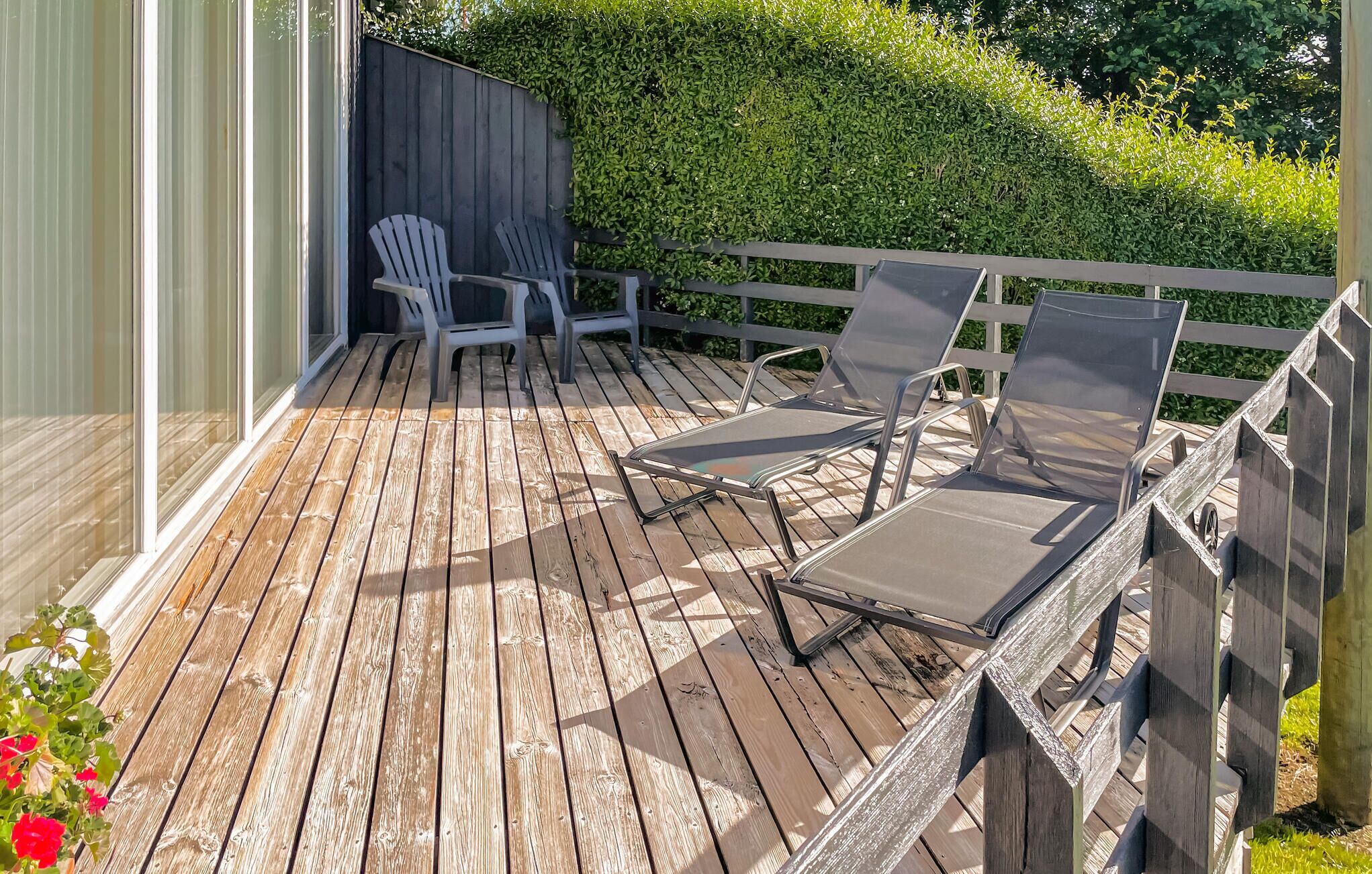 Een houten terras met twee Adirondack-stoelen en een ligstoel.