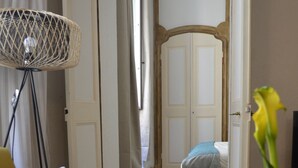 Een kamer met een gele fauteuil, een vloerlamp, een bed met een blauwe deken en een plant in een pot.