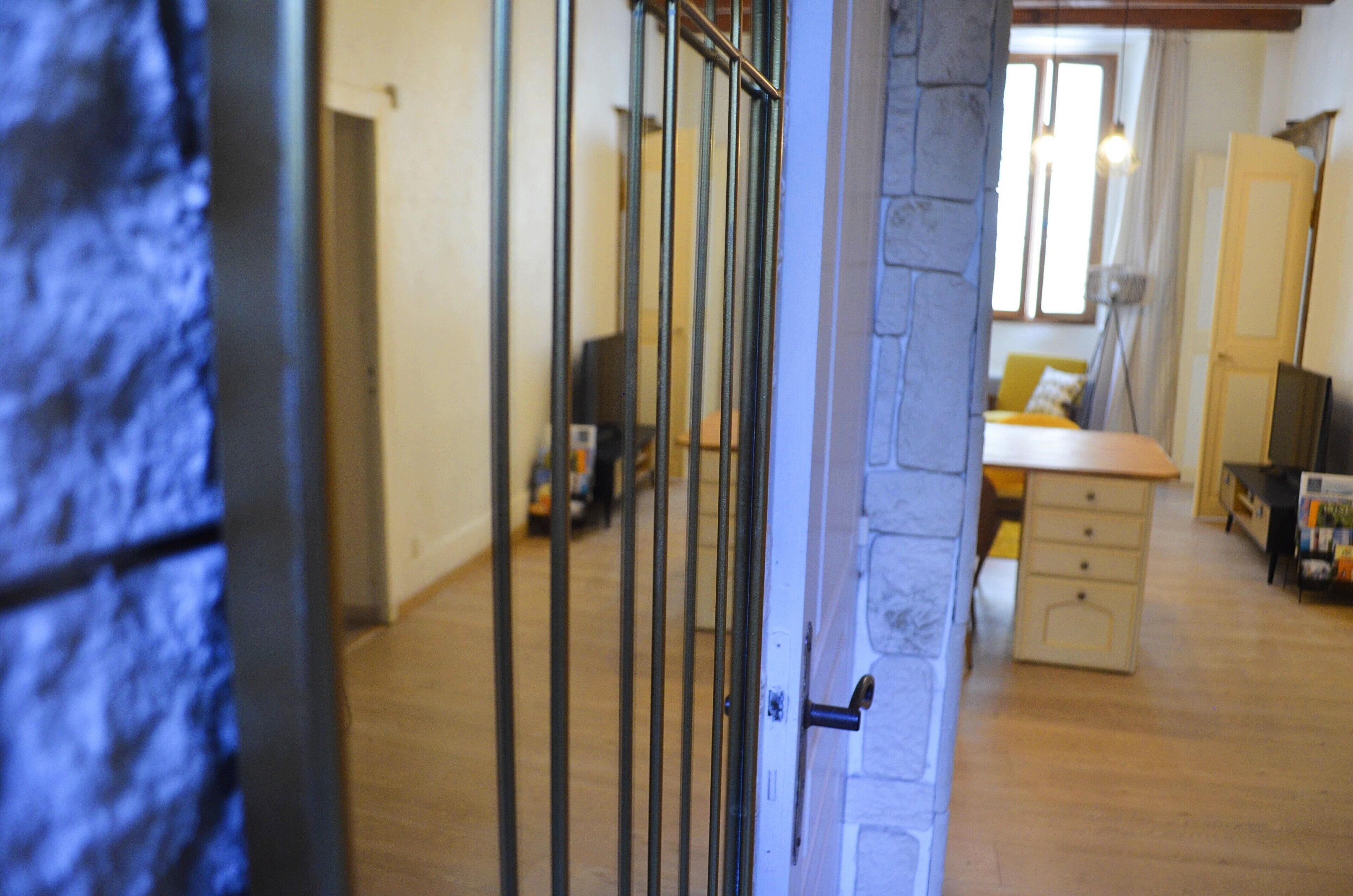 A hallway with a stone wall, a wooden floor, and a door with metal bars.