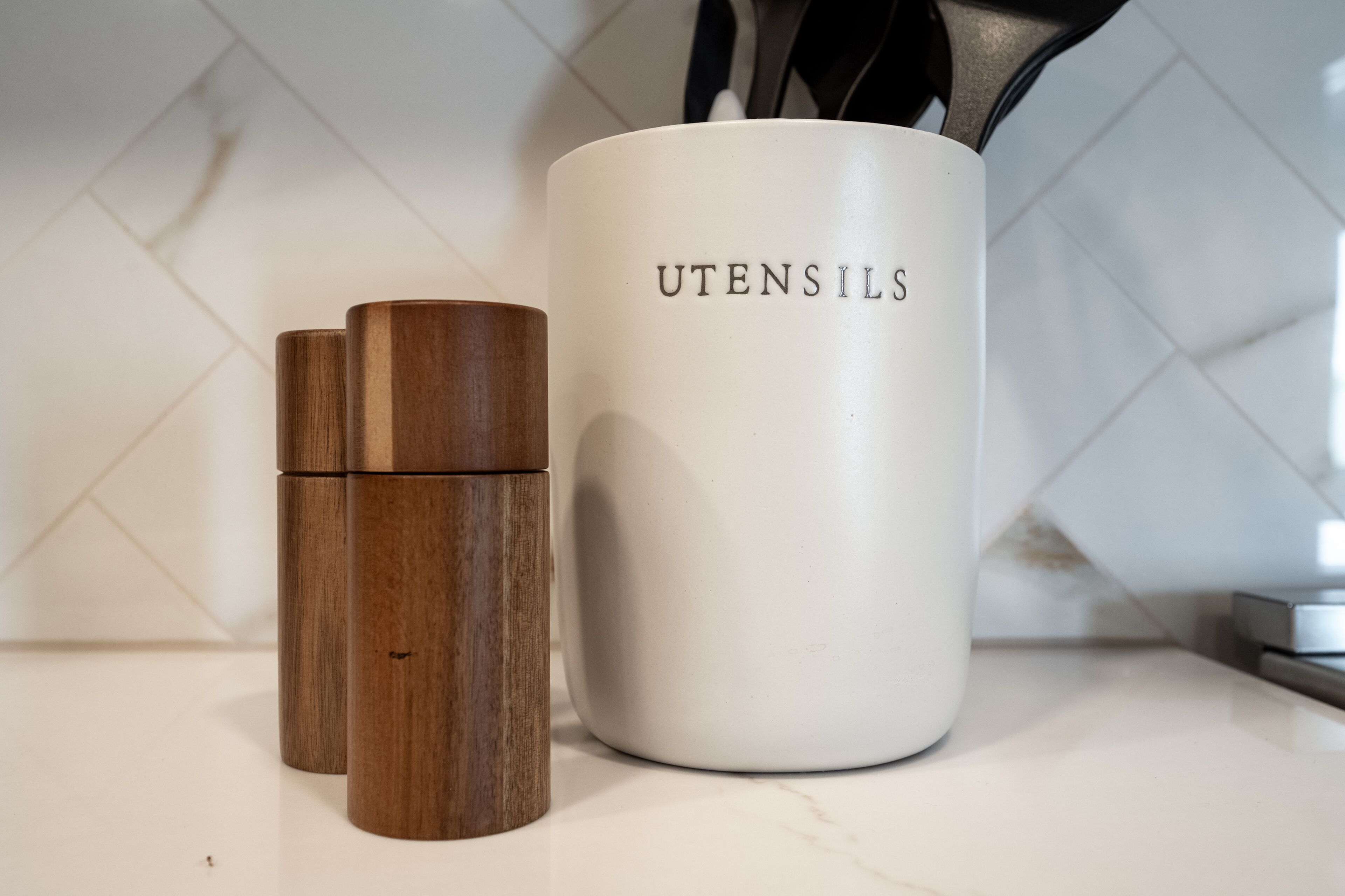 A kitchen counter with a white mug labeled "UTENSILS" and two wooden containers.