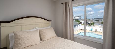 A bedroom with a large bed, a window with a view of a swimming pool, and a white headboard.