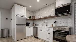A modern kitchen with white cabinets, a stainless steel refrigerator, a built-in oven, and a microwave.