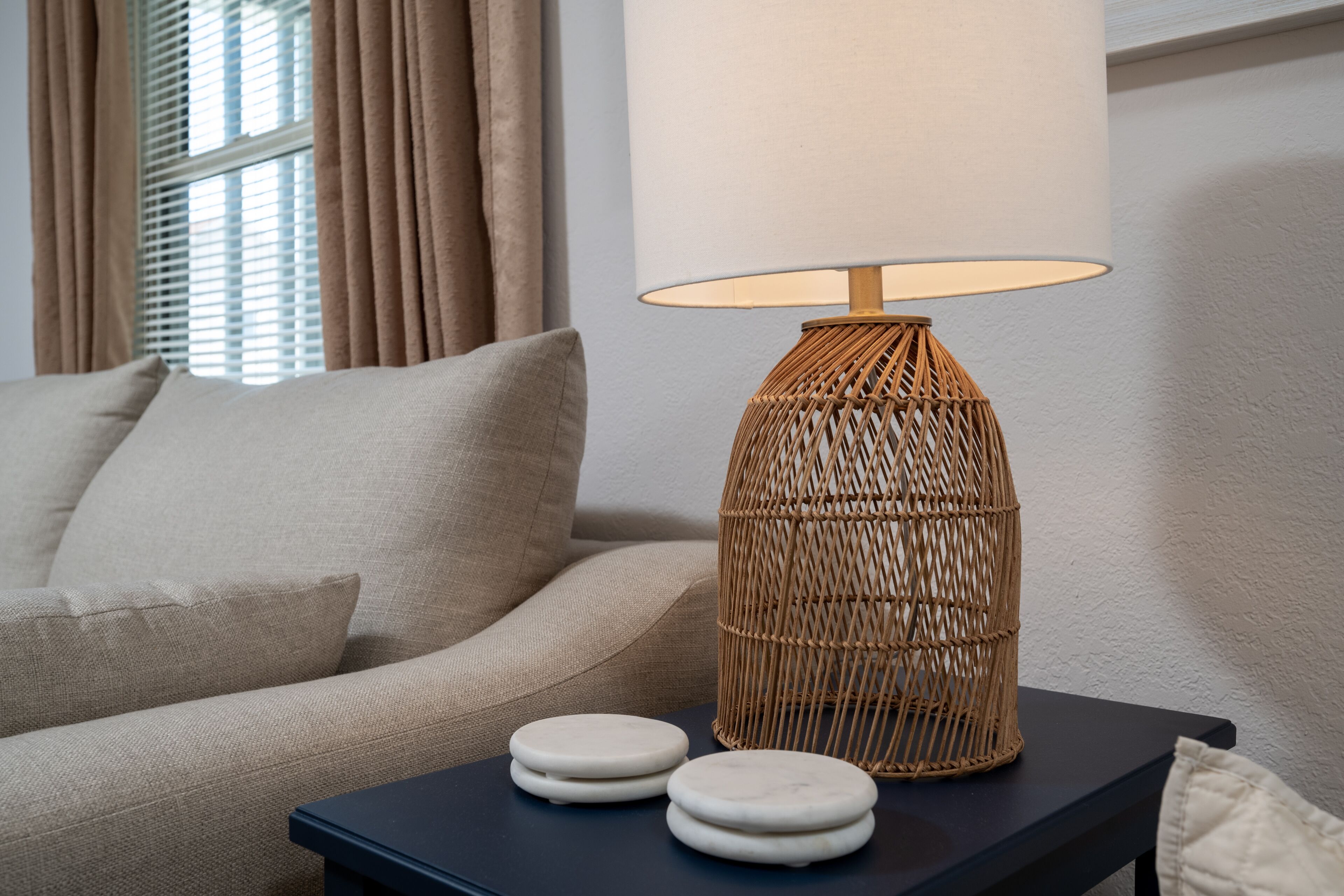 Ein modernes Wohnzimmer mit einem dunkelblauen Beistelltisch, einer Korbtasche-Lampe und einem beigen Sofa.