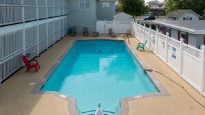 A rectangular pool with a white deck, surrounded by a white fence and a few lounge chairs.