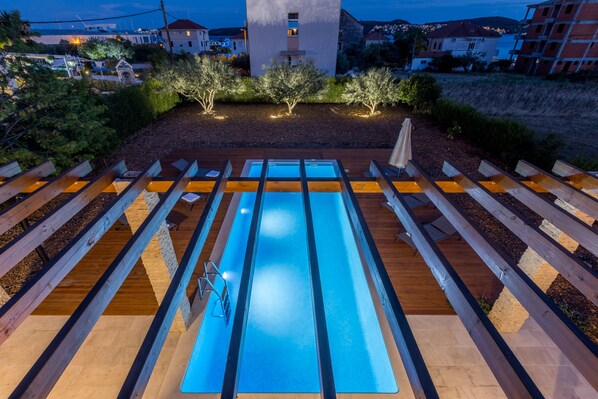 A swimming pool with wooden deck railings, surrounded by landscaped greenery and a view of nearby buildings. - Villa Trogir SAVE 20 percent on Split-villas com
(Seget Donji)