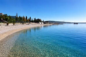 A clear beach with pebbles, a few buildings, and a boat in the distance. - Villa Trogir SAVE 20 percent on Split-villas com
(Seget Donji)