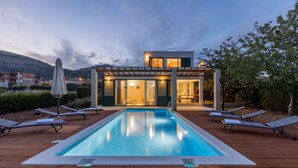 Ett modernt hus med en swimmingpool, ett trädäck och solstolar.