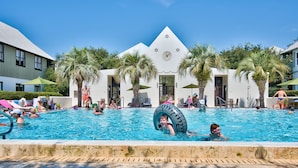 Un espace piscine agrémenté de palmiers, une horloge et un bâtiment à la façade blanche.